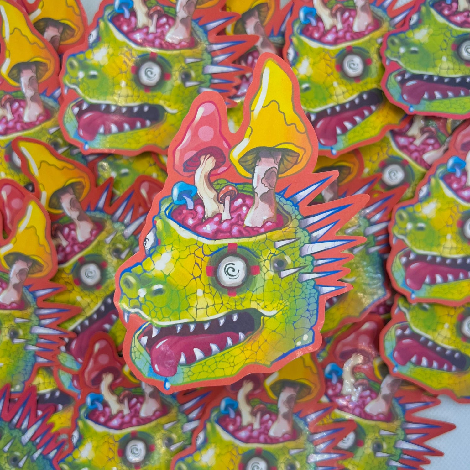 A pile of colorful novelty stickers featuring a green spiky monster head with children riding on its back under yellow mushrooms, set against a light gray background.