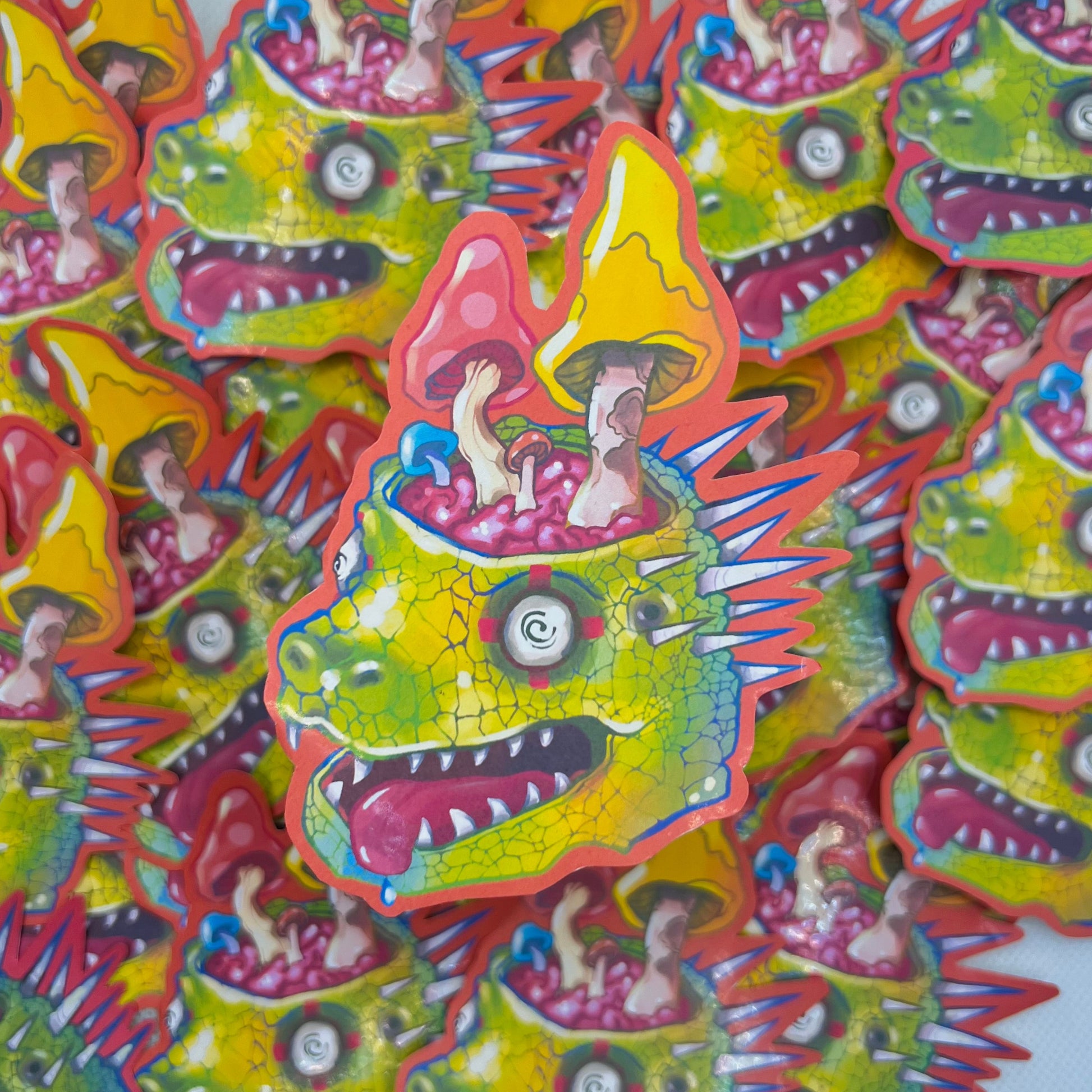 A pile of colorful novelty stickers featuring a green spiky monster head with children riding on its back under yellow mushrooms, set against a light gray background.