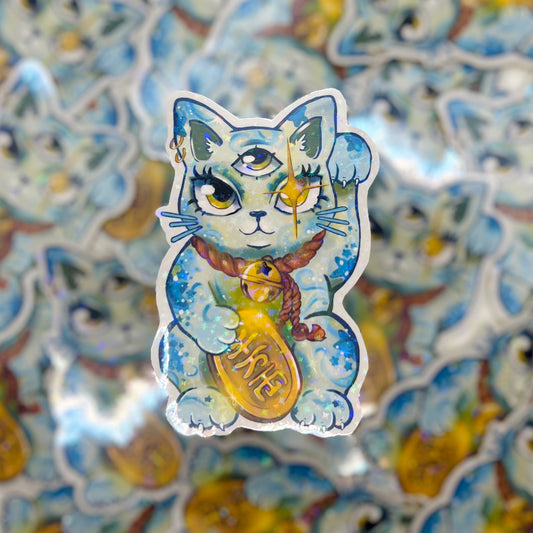 A die-cut sticker featuring a blue and white watercolor-style cat with one eye open, holding a gold coin that reads 'HURIE', set against a blurred background of similar stickers.